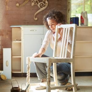 Vrouw die bezig is met het schuren van een oude stoel