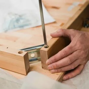 Verschillende stukken hout en een hand die en schroef in hout draait"