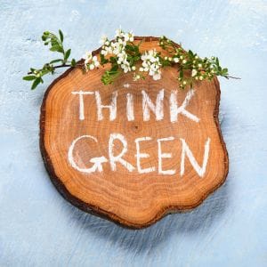 Houten schijf met witte tekst Think Green en een tak met groene blaadjes en witte bloemetjes aan de bovenkant